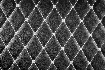 close-up of a black leather surface with a diamond-shaped stitching pattern. The deep, rich color of the leather and the intricate stitching create a luxurious and sophisticated look backgroundの写真素材