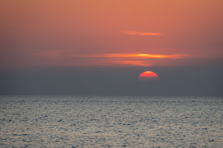 tranquil scene of a sunset slowly disappearing below the horizon, casting soft, pink and orange hues over the calm ocean.の写真素材