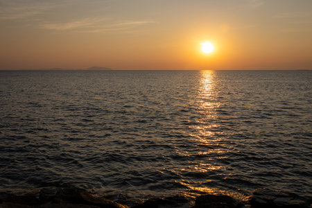 serene sunset view over the ocean, with the sun casting a warm golden reflection on the water's surfaceの写真素材