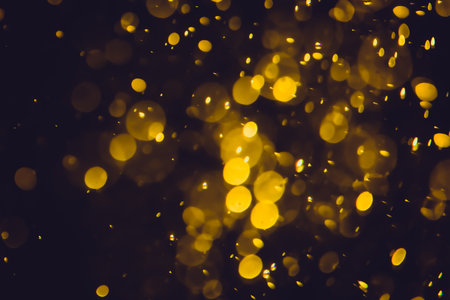 Defocused golden bokeh lights of different sizes and colors on a dark background.の写真素材