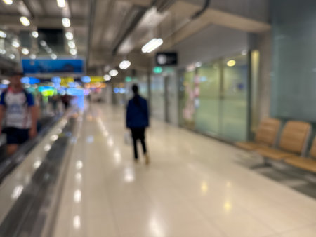 blurred image of travelers walking along an airport terminal with a moving walkway and modern architectural details.の写真素材