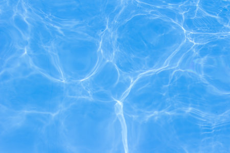 Clear blue swimming pool water with sunlight reflections creating abstract patterns and ripples.