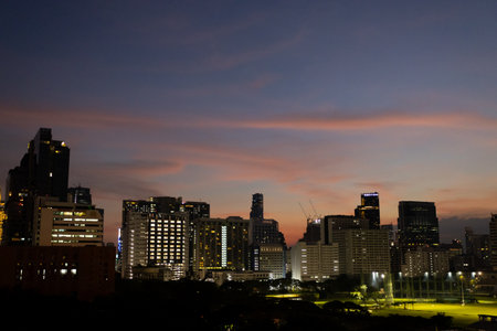 Dusk cityscape with vibrant sunset sky over urban skyline, illuminated buildings, and soft, colorful clouds reflecting evening light.の写真素材