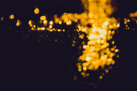 Abstract blurred golden bokeh lights against a dark background creating a warm and festive atmosphere.の写真素材