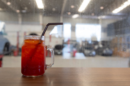 refreshing iced red beverage served in a mason jar with a black straw, placed on a wooden table. The...