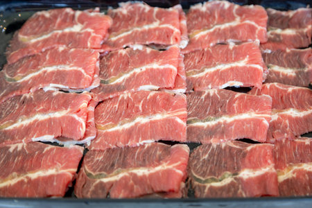 A close-up shot showcasing the intricate marbling of raw beef slices. The vibrant red hues contrast beautifully with the delicate streaks of white fatの写真素材