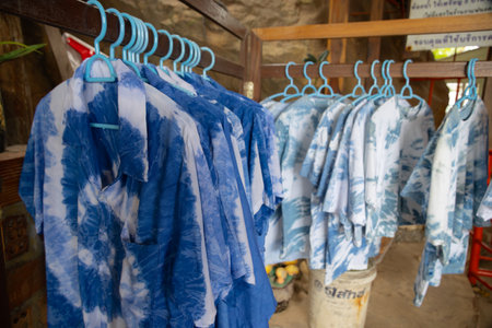 close-up shot of tie-dye t-shirts hanging on light blue plastic hangers. The shirts feature a soft, pastel tie-dye pattern. The hangers are neatly arranged on a wooden rackの写真素材