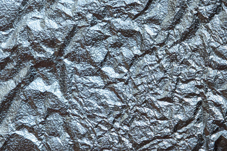 close-up of crumpled silver foil, revealing a chaotic and abstract pattern. The metallic sheen and irregular surface create a dynamic and visually striking image.の写真素材