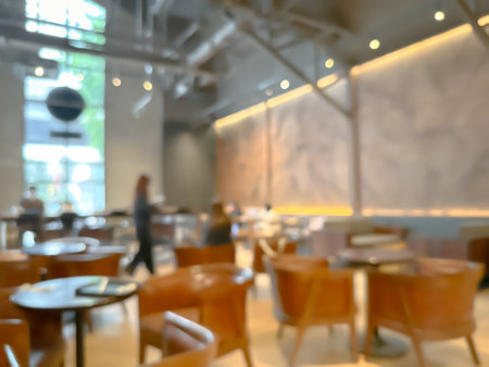 Blurred interior of a modern cafe with wooden chairs and tables, warm lighting, and large windows.の写真素材