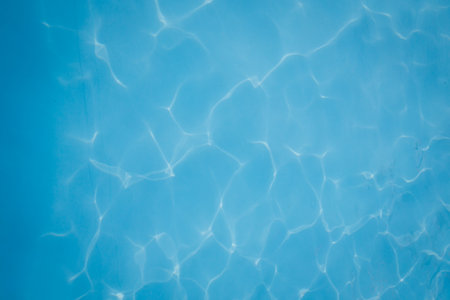 Close-up of clear blue swimming pool water with gentle sunlight reflections creating abstract patterns.の写真素材