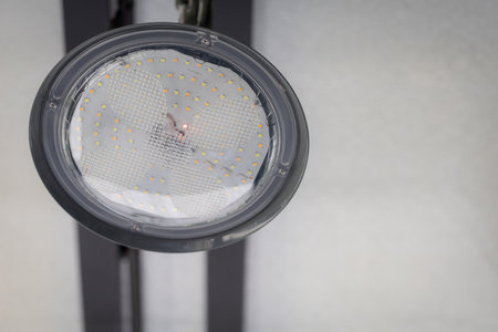 Hanging industrial light fixture with glass cover, metal frame ceiling, blurred background.の写真素材