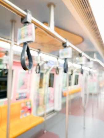 Blurred view of an empty subway train interior with bright yellow seats and stainless steel poles....
