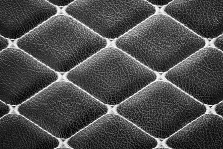 close-up of a black leather surface with a diamond-shaped stitching pattern. The deep, rich color of the leather and the intricate stitching create a luxurious and sophisticated look backgroundの写真素材