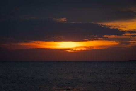 The sun dips below the horizon, casting a golden glow over the calm sea. A gentle breeze ruffles the water as a lone sailboat glides peacefully across the bay. Seagulls cry overhead, adding to the tranquil atmosphere.の写真素材