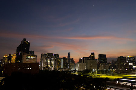 Dusk cityscape with vibrant sunset sky over urban skyline, illuminated buildings, and soft, colorful clouds reflecting evening light.の写真素材