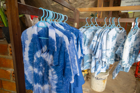 close-up shot of tie-dye t-shirts hanging on light blue plastic hangers. The shirts feature a soft, pastel tie-dye pattern. The hangers are neatly arranged on a wooden rackの写真素材