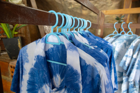 close-up shot of tie-dye t-shirts hanging on light blue plastic hangers. The shirts feature a soft,...