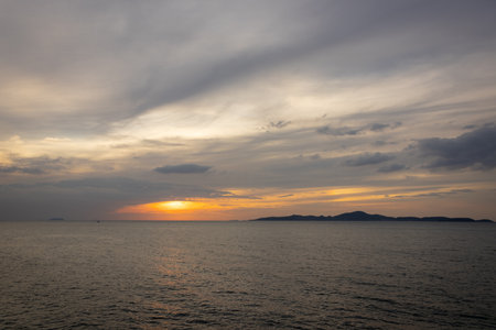 The sun dips below the horizon, casting a golden glow over the calm sea. A gentle breeze ruffles the water as a lone sailboat glides peacefully across the bay. Adding to the tranquil atmosphere.の写真素材