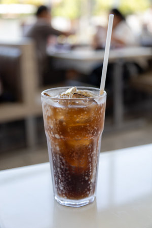 A glass of ice-cold cola sits on a table, condensation glistening on the glass. The bubbles fizz invitingly, promising a refreshing drink.の写真素材