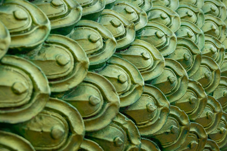 close-up of ornate, metallic green and gold scales, reminiscent of a dragon or the mythical Naga serpent in Thai art. The intricate pattern and shimmering texture create a visually captivating backgroundの写真素材