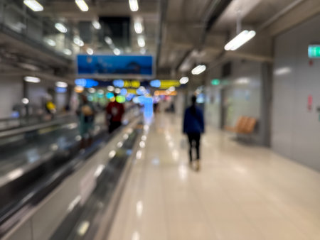 blurred image of travelers walking along an airport terminal with a moving walkway and modern architectural details.の写真素材