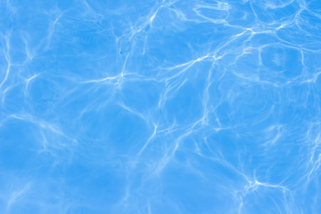 Clear blue swimming pool water with sunlight reflections creating abstract patterns and ripples.の写真素材