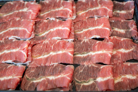 A close-up shot showcasing the intricate marbling of raw beef slices. The vibrant red hues contrast beautifully with the delicate streaks of white fatの写真素材