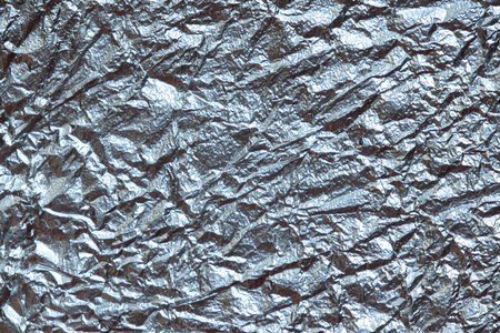 close-up of crumpled silver foil, revealing a chaotic and abstract pattern. The metallic sheen and irregular surface create a dynamic and visually striking image.の写真素材