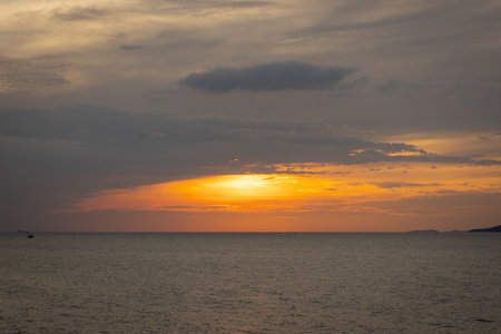 The sun dips below the horizon, casting a golden glow over the calm sea. A gentle breeze ruffles the water as a lone sailboat glides peacefully across the bay. Seagulls cry overhead, adding to the tranquil atmosphere.の写真素材