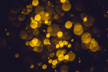 Defocused golden bokeh lights of different sizes and colors on a dark background.の写真素材
