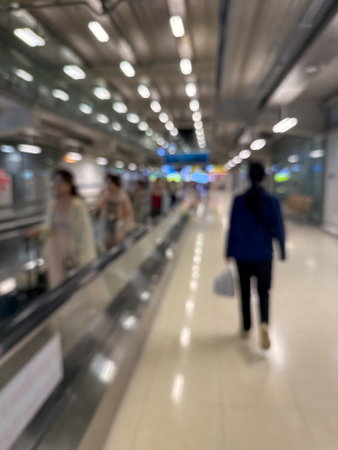 blurred image of travelers walking along an airport terminal with a moving walkway and modern architectural details.の写真素材