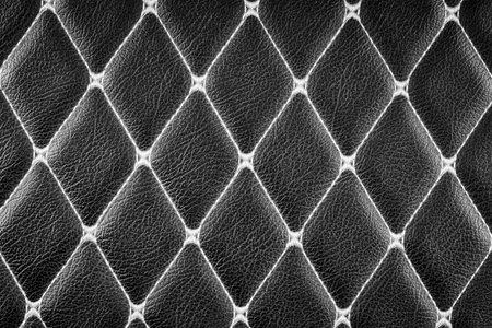 close-up of a black leather surface with a diamond-shaped stitching pattern. The deep, rich color of the leather and the intricate stitching create a luxurious and sophisticated look backgroundの写真素材