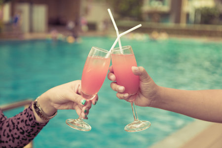 Couple holding champagne glasses near the swimming pool. Focus on the glassesの写真素材