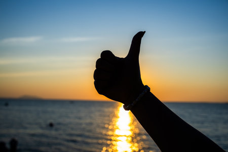Silhouette of hand showing thumbs up on the sea background.の写真素材