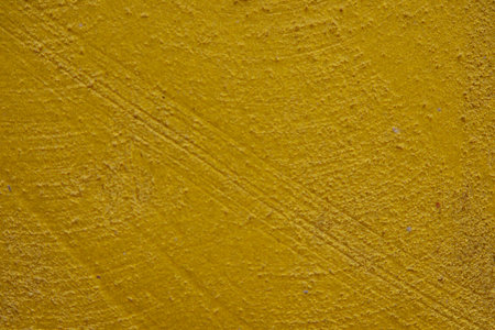 close-up shot of a textured gold yellow concrete surface. The rough and slightly uneven texture, along with subtle variations in the gold yellow hue, creates a visually interesting background. Some subtle horizontal lines are visible.の写真素材