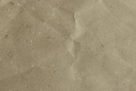 Close-up of a crumpled, light brown kraft paper texture. Its earthy tone and subtle wrinkles create an organic, rustic background.の写真素材
