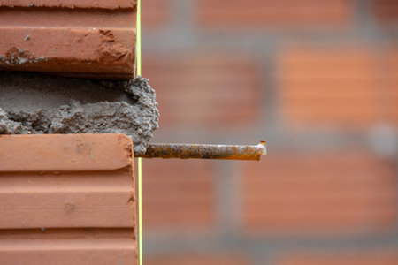 A close-up of a construction site showing a corner of a brick wall with exposed rebar and fresh...