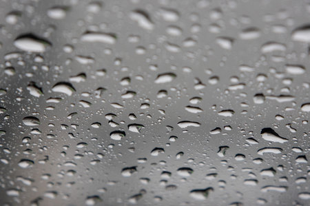 close-up, full-frame shot of numerous water droplets of varying sizes clinging to a glass surface,...
