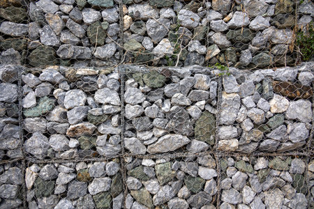 gabion wall, showcasing the texture of the grey stones and the wire mesh. The image highlights the...