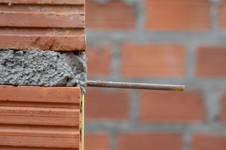 A close-up of a construction site showing a corner of a brick wall with exposed rebar and fresh mortar. The focus is on the building process.の写真素材