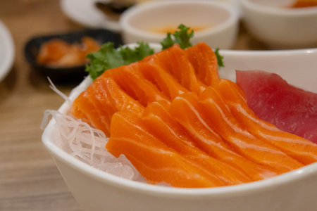 close-up of a white bowl with fresh, raw slices of bright orange salmon and red tuna sashimi, served on a bed of ice.の写真素材