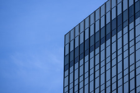 A section of a modern building with many rectangular glass windows reflecting the clear, bright blue sky.の写真素材