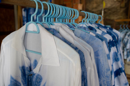 close-up shot of tie-dye t-shirts hanging on light blue plastic hangers. The shirts feature a soft, pastel tie-dye pattern. The hangers are neatly arranged on a wooden rackの写真素材
