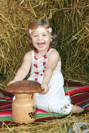 The joyful girl sits with bread near a straw stackの写真素材