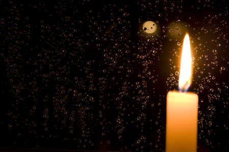 Rain drops reflect light of a burning candle in glass at nightの写真素材