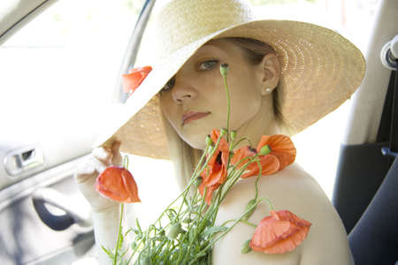 The woman in a hat with red poppies sits in the carの写真素材