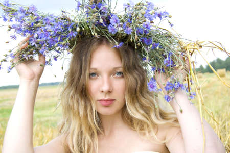 tired woman sits on straw in the summer and on a head a wreath from cornflowersの写真素材