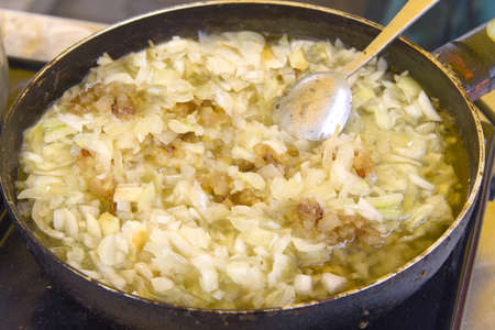 Frying pan on an electric stove with a spoon, fried fat with onionsの写真素材