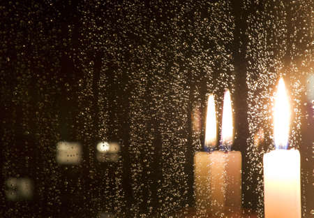 Rain drops reflect light of a burning candle in glass at nightの写真素材