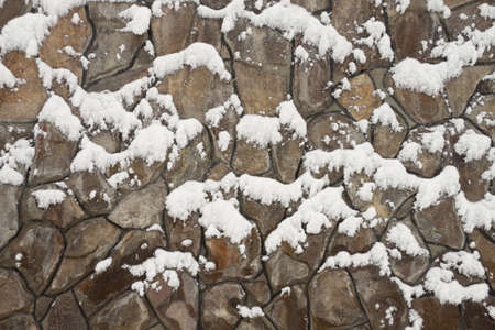 Wall from multi-coloured stones of the various form fastened by clay under snow